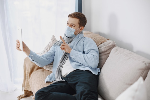 Mann in einer medizinischen Maske. Mann, der zu Hause im Wohnzimmer sitzt. Kerl, der es genießt, in Quarantäne zu lernen.