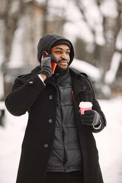 Mann in einer Winterstadt. Mann in einem schwarzen Mantel. Mann mit Kaffee und Telefon.