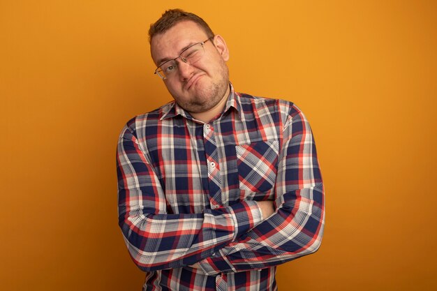 Mann in Gläsern und kariertem Hemd, das mit skeptischem Ausdruck beiseite schaut, der ironischen Mund macht, der über orange Wand steht