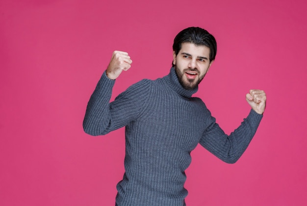 Mann in grauem Pullover demonstriert seine Fäuste und fühlt sich mächtig.