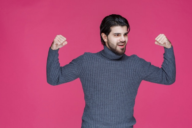 Mann in grauem Pullover demonstriert seine Fäuste und fühlt sich mächtig.