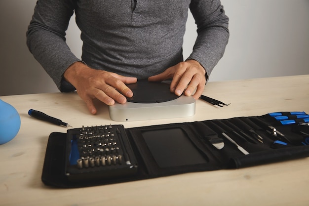 Mann in grauem T-Shirt schließt den Computer, den er repariert hat, seine Werkzeuge vor sich auf dem Tisch