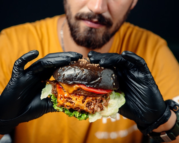 Kostenloses Foto mann in schwarzen handschuhen hält einen saftigen cheeseburger in schwarzbrot