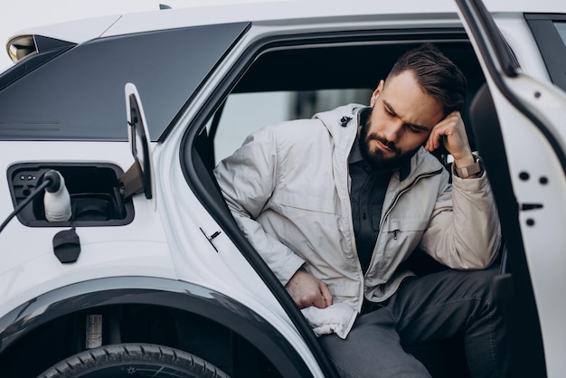 Kostenloses Foto mann lädt elektroauto am haus auf