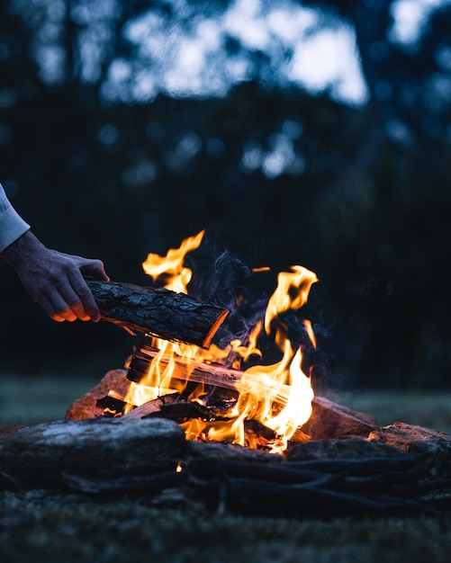 Mann legt abends einen Holzscheit in ein Lagerfeuer