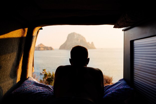 Kostenloses Foto mann liegt in einem wohnwagen und genießt den sonnenuntergang am strand