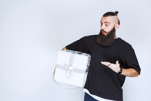 Mann mit Bart, der eine weiß-blaue Geschenkbox hält und enttäuscht aussieht.