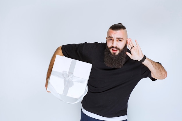 Mann mit Bart, der eine weiße blaue Geschenkbox hält und aufmerksam zuhört.