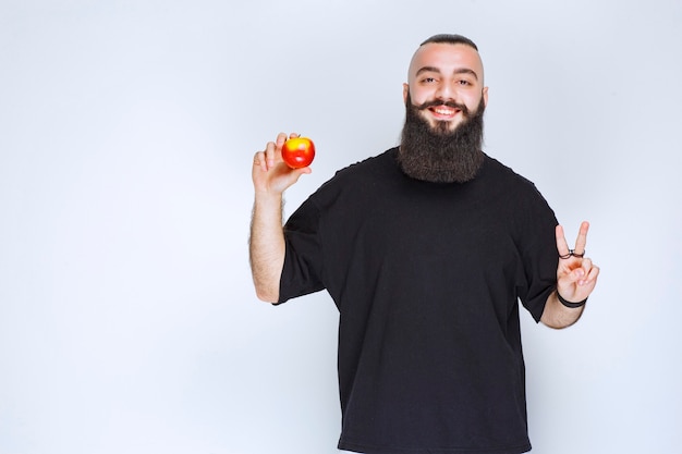 Mann mit Bart, der einen roten Apfel oder Pfirsich hält und den Geschmack genießt.