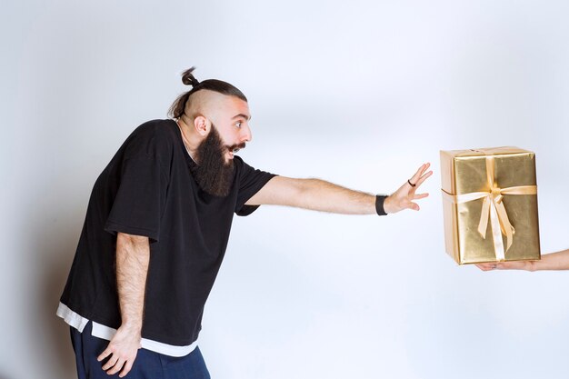 Kostenloses Foto mann mit bart, der sich nach vorne sehnt, um eine goldene geschenkbox zu nehmen, die ihm angeboten wird.