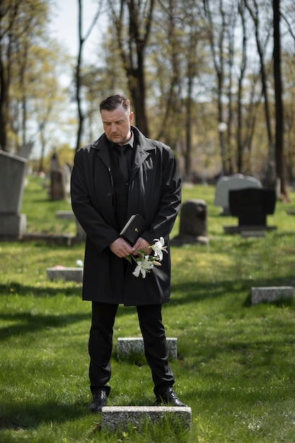 Mann mit Blumen und Bibel auf dem Friedhof