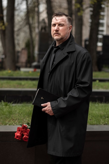 Kostenloses Foto mann mit blumen und bibel auf dem friedhof