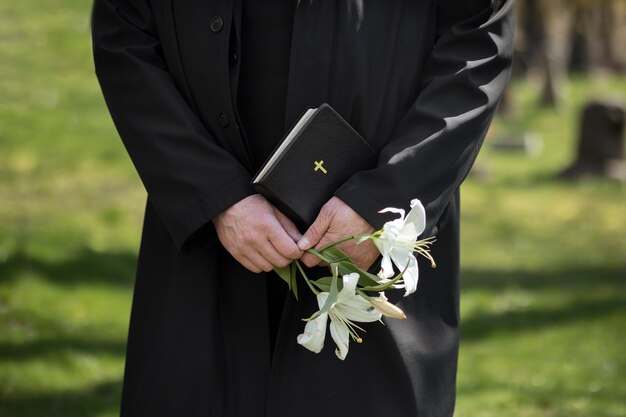 Mann mit Blumen und Bibel auf dem Friedhof