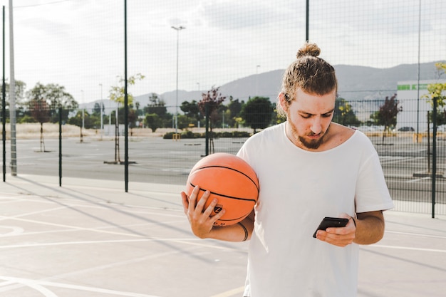 Kostenloses Foto mann mit dem backetball, der vor gericht handy betrachtet