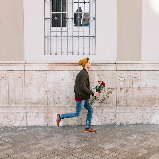 Kostenloses Foto mann mit dem blumenstrauß, der auf straße läuft