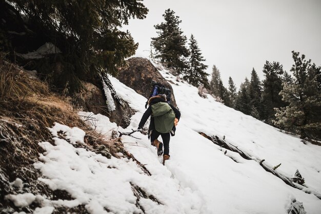 Mann mit dem Brennholz, das schneebedeckten Hügel klettert