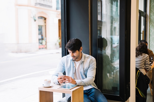 Mann mit dem Smartphone, der im Café sitzt