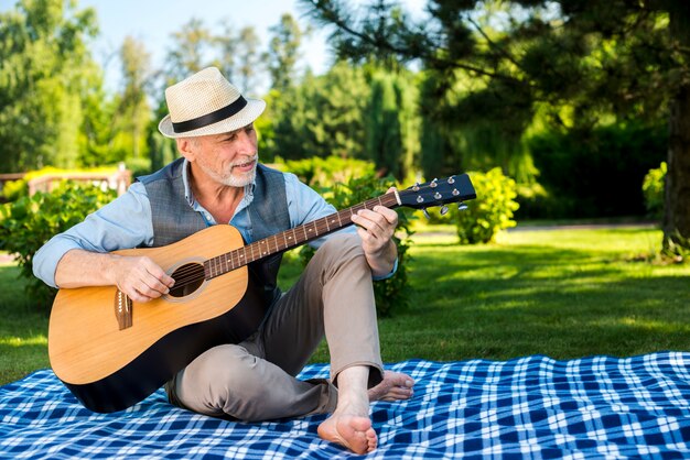 Mann mit der Gitarre, die auf einer Picknickdecke sitzt