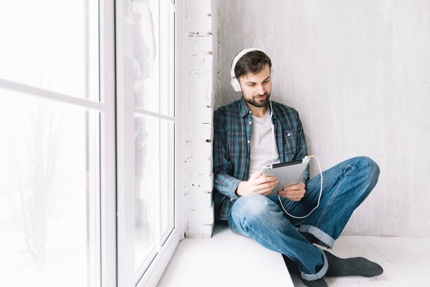 Mann mit der Tablette, die nahe Fenster sich entspannt