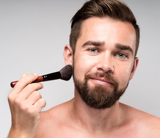 Mann mit einem Make-up Pinsel auf seinem Gesicht