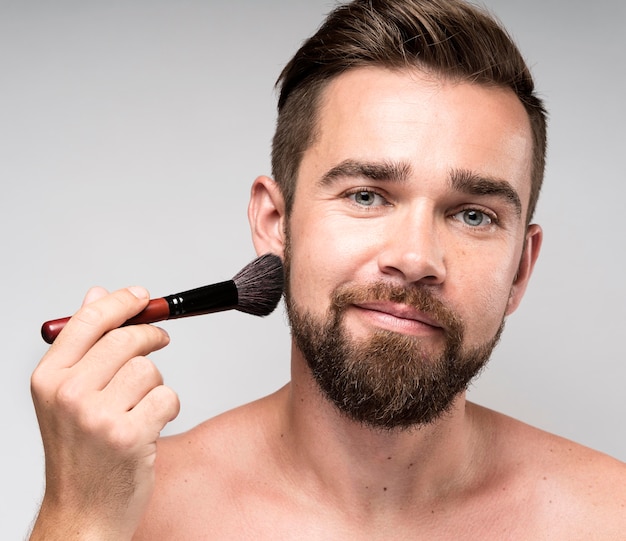 Mann mit einem Make-up Pinsel auf seinem Gesicht