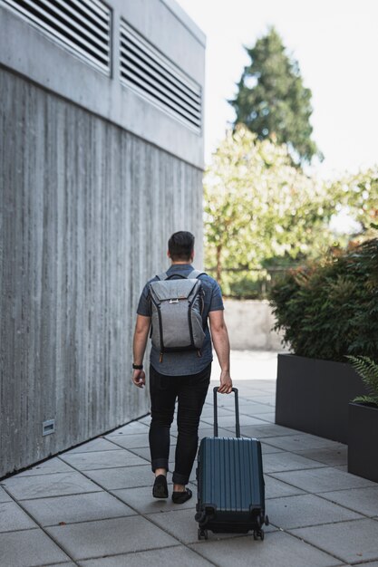 Mann mit einem Rucksack, der einen Koffer führt