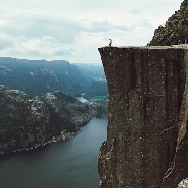 Mann mit einer gelben Jacke posiert auf der Oberseite des Felsens