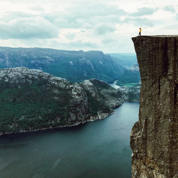 Kostenloses Foto mann mit einer gelben jacke posiert auf der oberseite des felsens