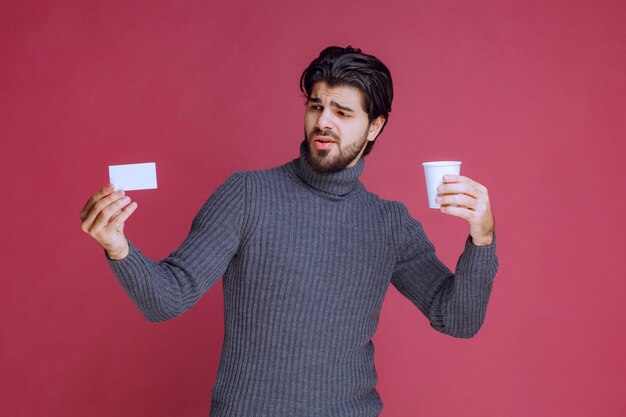 Mann mit einer Kaffeetasse, die seine Rechnung oder Visitenkarte zeigt.