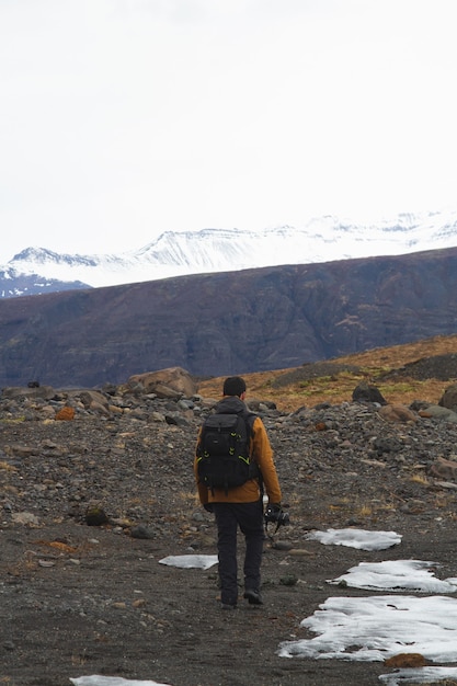 Mann mit einer Kamera, die durch felsige Berge wandert, die im Schnee in Island bedeckt sind