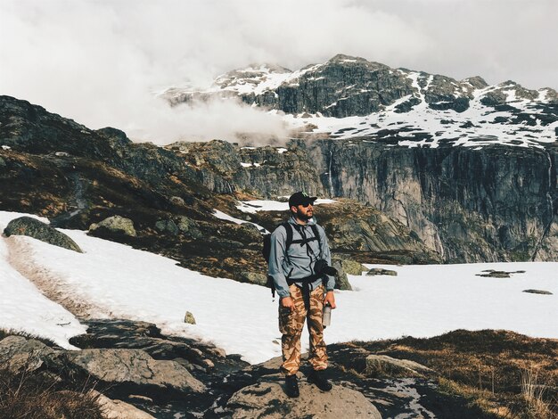 Mann mit einer Kamera und Rucksack steht vor den Bergen mit Schnee bedeckt