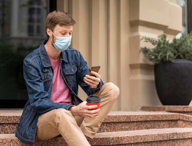 Mann mit Gesichtsmaske, der sein Telefon überprüft