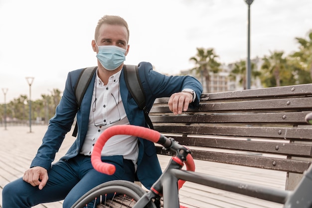Mann mit Gesichtsmaske sitzt auf einer Bank neben seinem Fahrrad im Freien