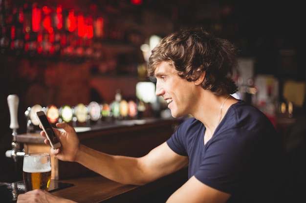 Mann mit Glas Bier unter Verwendung des Mobiltelefons im Zähler