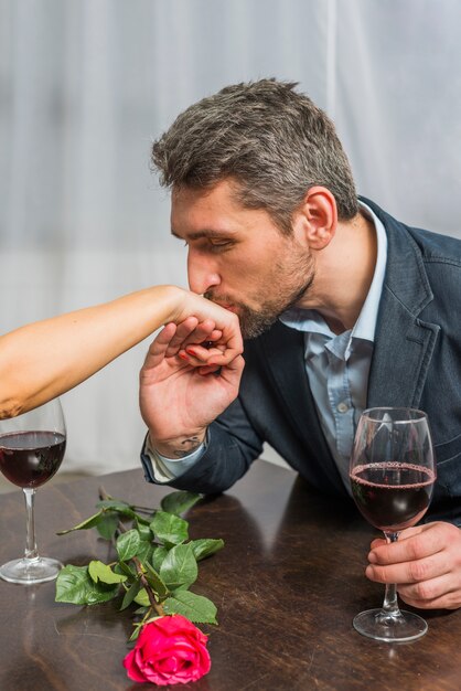 Kostenloses Foto mann mit glas der küssenden hand des weins der frau bei tisch mit stieg