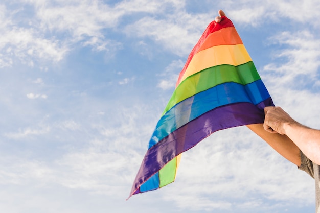 Mann mit großer Flagge in den LGBT-Farben und im blauen Himmel