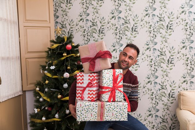 Mann mit Haufen von Geschenken nahe Weihnachtsbaum