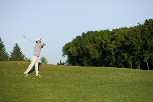 Mann mit Hut beim professionellen Golfspielen in der Luft. Golfspieler, der Golfschlag mit Verein auf dem Kurs schlägt.