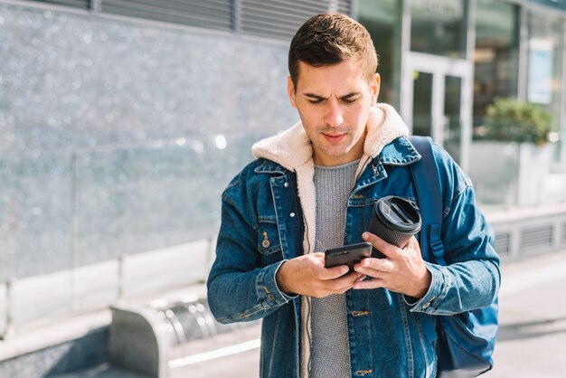 Mann mit Kaffee und Smartphone in der städtischen Umgebung