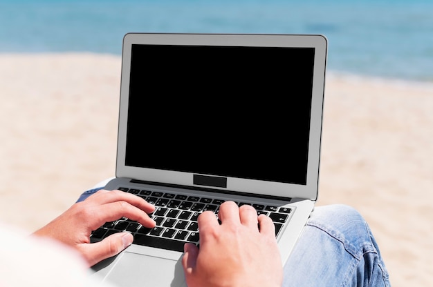 Mann mit Laptop, der am Strand arbeitet