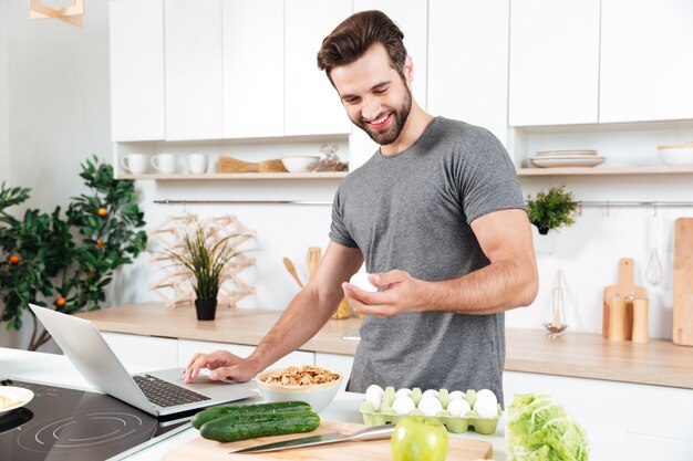 Mann mit Laptop, der Essen an der Küche vorbereitet