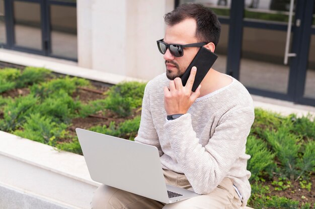 Mann mit Laptop und Smartphone, die draußen arbeiten