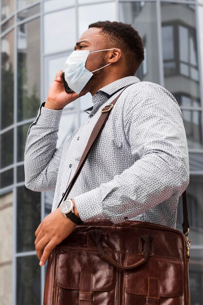 Kostenloses Foto mann mit maske auf dem weg zur arbeit während der pandemie und am telefon sprechen