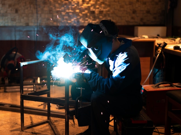 Mann mit Maskenschweißen von Metall im Atelier