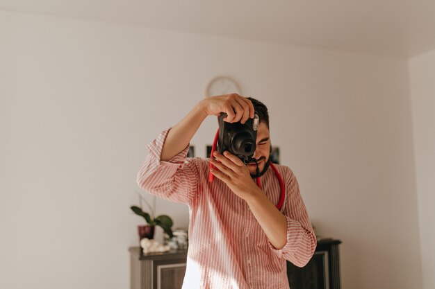 Mann mit Ring am Finger macht Foto vor der Kamera. Schnappschuss von Brunet Kerl in gestreiftem Outfit in geräumiger Wohnung.