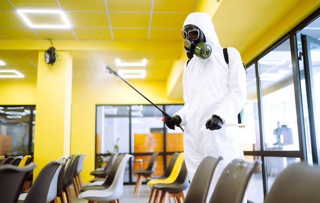 Mann mit schutzanzug, der die montagehalle mit sprühchemikalien desinfiziert, um das coronavirus zu verhindern.
