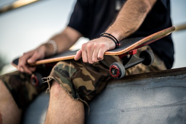 Mann mit schwarzem T-Shirt und Shorts hält ein schwarzes Skateboard auf den Knien