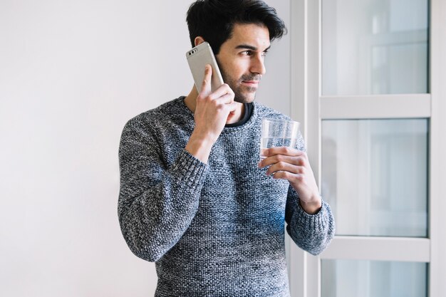 Mann mit Smartphone und Wasser nahe Fenster