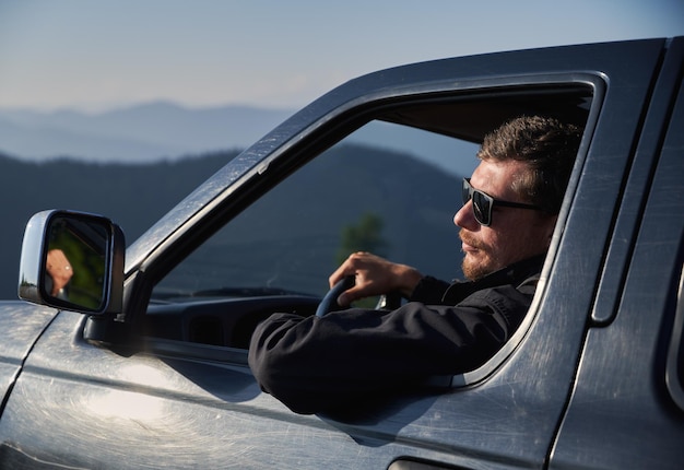 Mann mit Sonnenbrille, der schwarzes Auto in den Bergen fährt