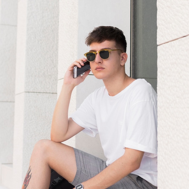 Kostenloses Foto mann mit sonnenbrille, die draußen am telefon spricht